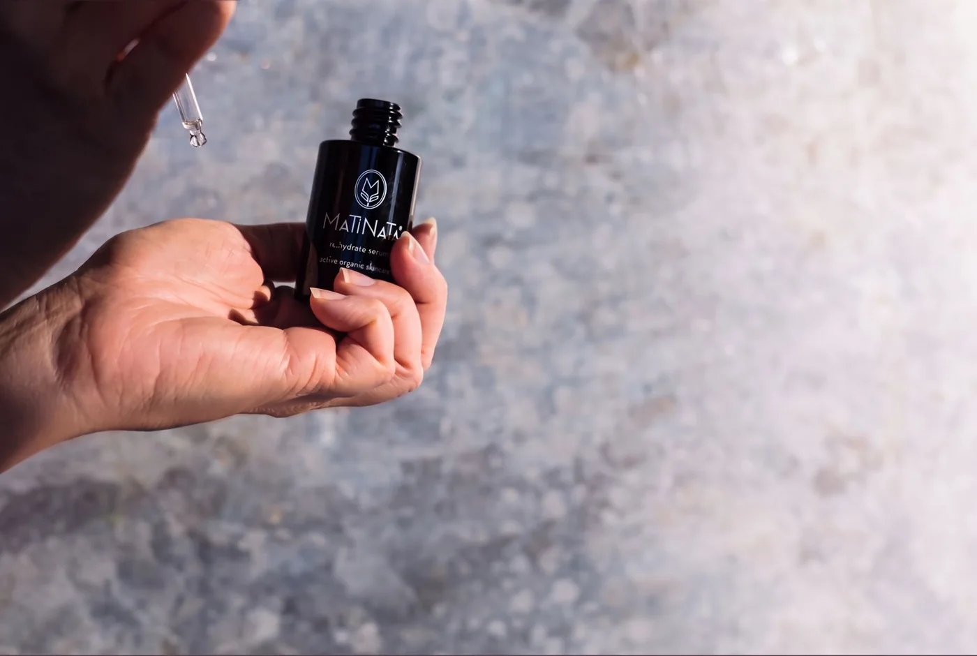 Hands holding a Matinata re.hydrate bottle and a dropper in natural light