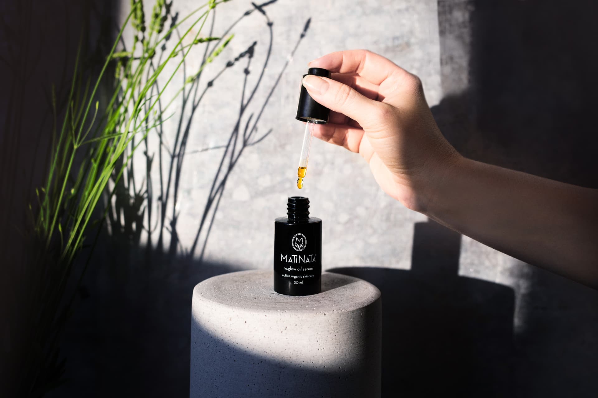 Matinata re.glow oil serum — hand lifting the dropper with golden oil in natural light