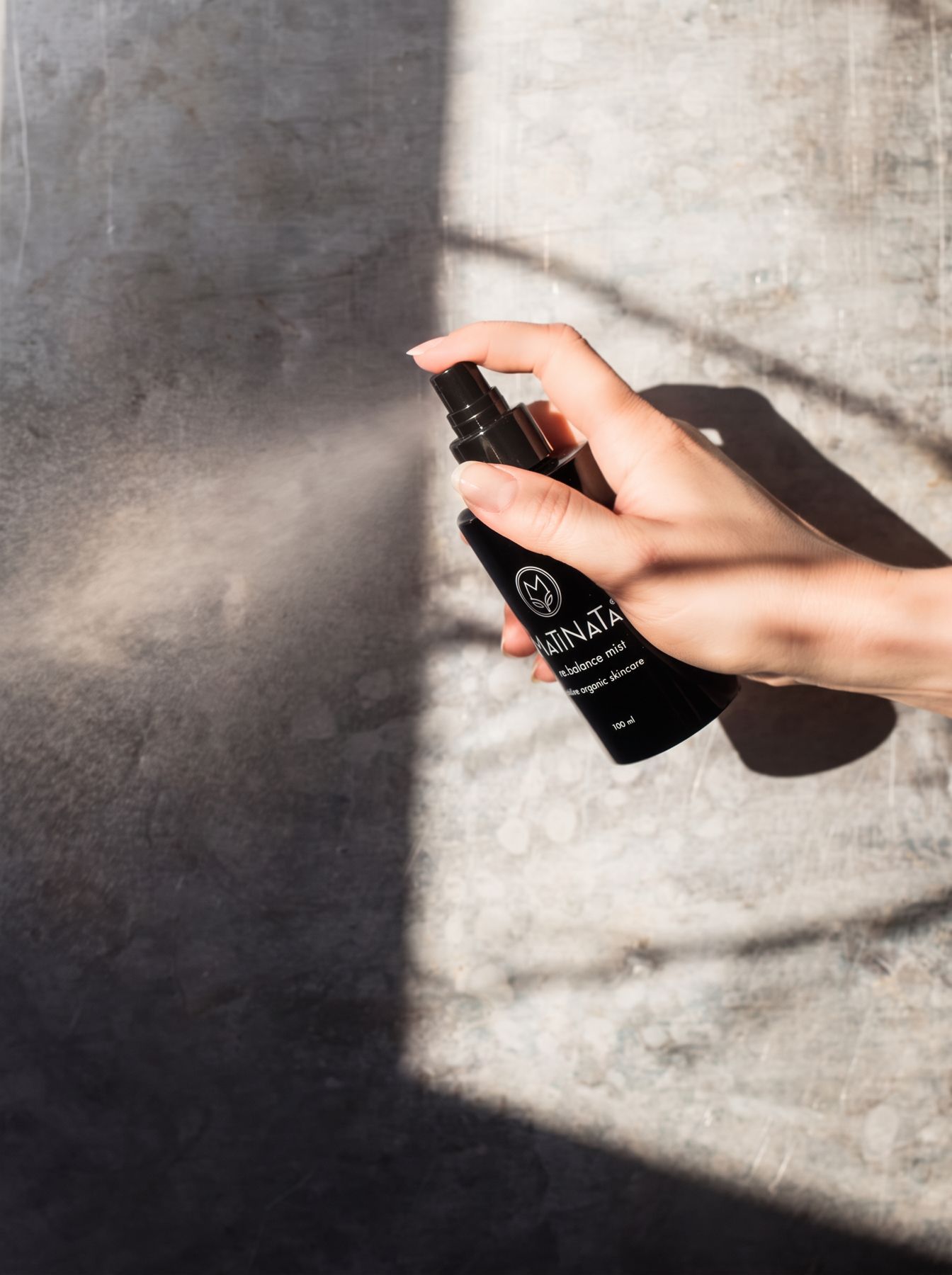 Matinata re.balance face mist being sprayed in sunlight against a stone wall