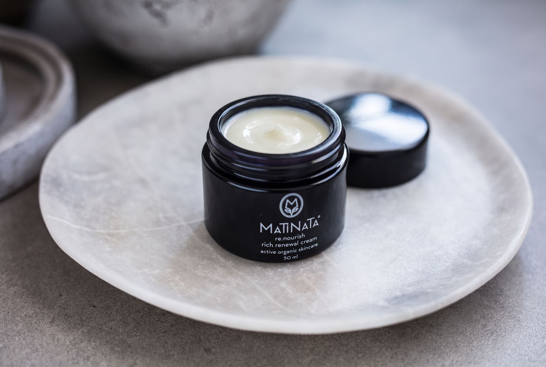 Matinata re.nourish rich renewal cream open on a marble plate, lid beside